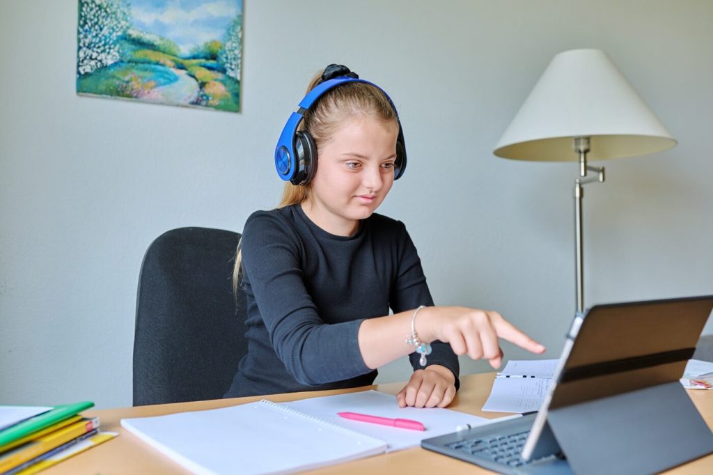 Élève portant un casque et travaillant sur une tablette, avec un cahier ouvert