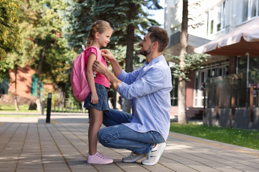Père aidant sa fille à préparer sa rentrée scolaire devant une école